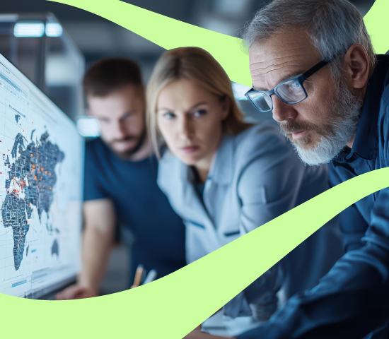 Three people in an office gathered around a computer screen showing a world map with data points. Faces are blurred.