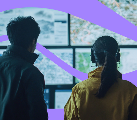 Emergency response team monitoring multiple data and map displays in a control room.