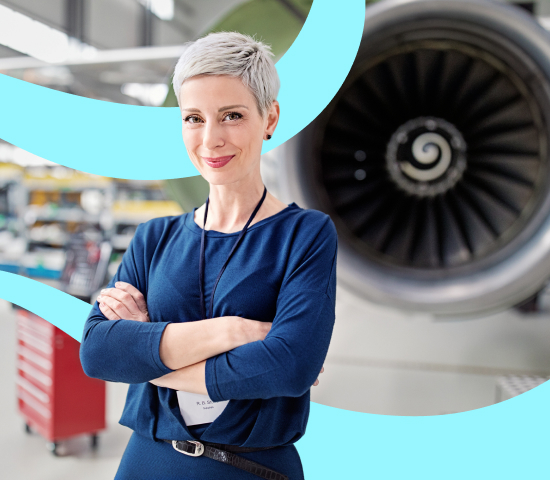 lady with short grey hair with folded arms standing in a large industrial building with large aircraft in the background