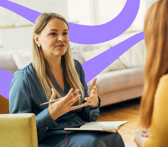 Two people seated and engaged in conversation, with one holding a pen and notebook, gesturing while speaking. Background includes a couch and abstract purple shapes.