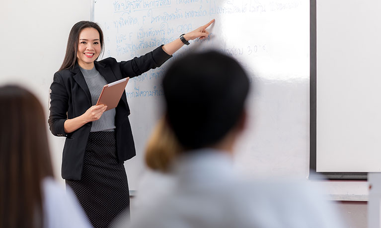 A middle-aged Asian woman teacher helping a student during on a class