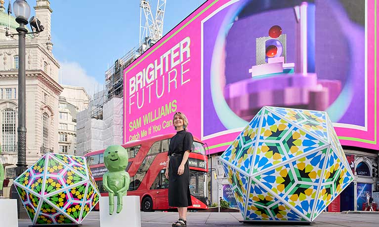 Sam at piccadilly circus in front of a big screen credit: Brighter Future Art of London 2022