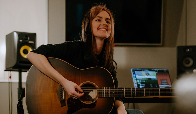 Emma McGann playing guitar in a recording studio