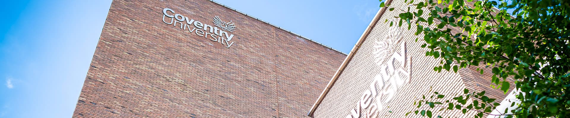 A Coventry University building on a sunny day with green leaves on the side