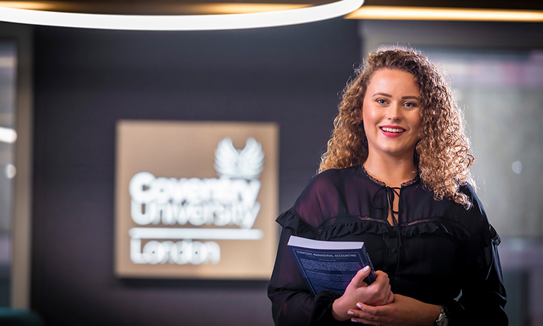 Coventry University London student Laura holding a book and smiling