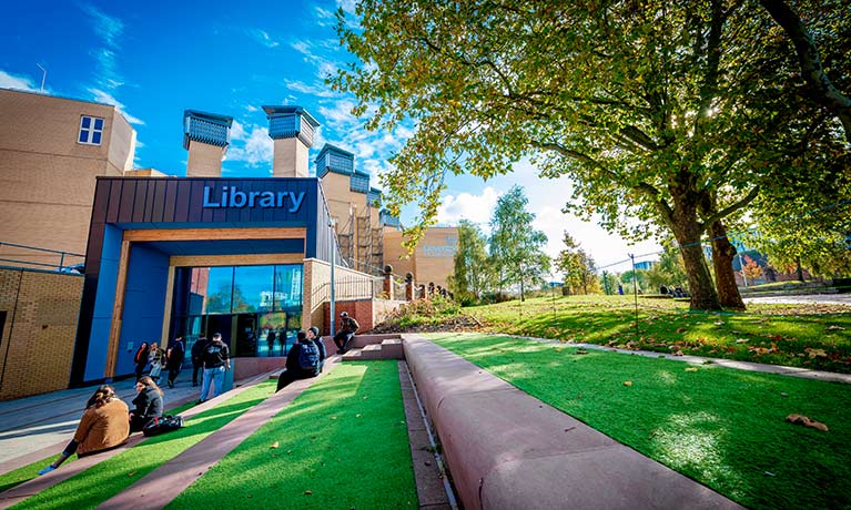 Students sitting outside the library on a sunny day