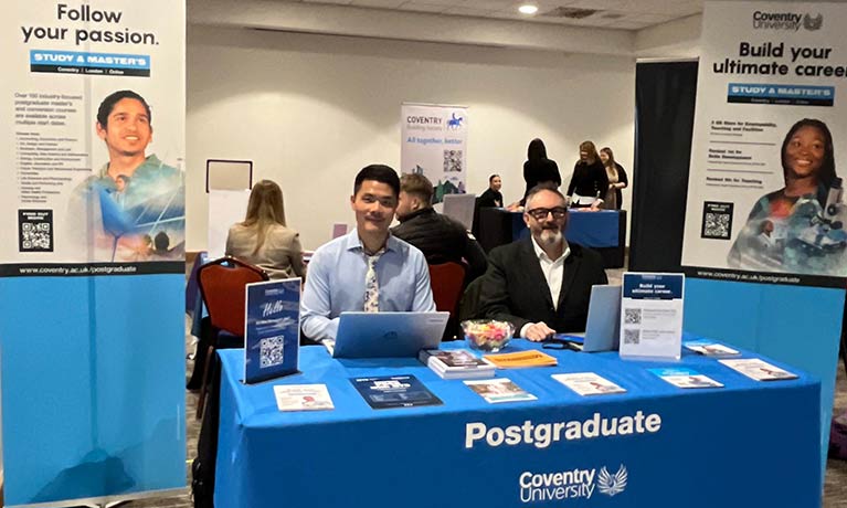 Postgraduate team sat at a stand at an event