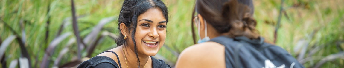 Two students with backpacks on, chatting outside