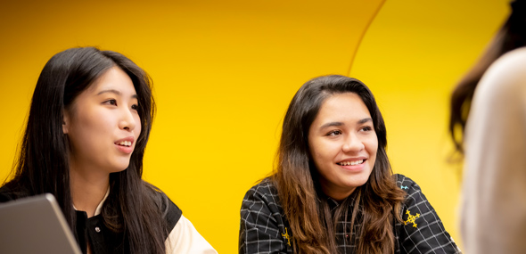 Two international students sat at a table with a laptop next to them.