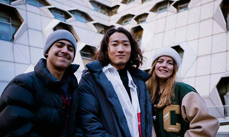 Three students in winter clothes outside the Sir Frank Whittle engineering building.