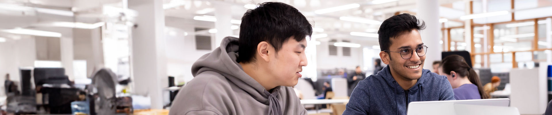 Two international students working on laptops in a large open study area.