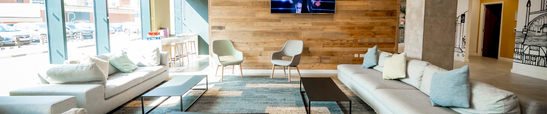 A comfortable communal area in a halls of accommodation, with long sofas, coffee tables and a flat screen television on the wall.