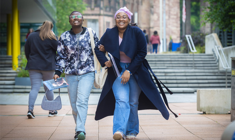 Two international students smiling and walking together outside The Hub on campus.