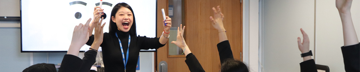 A Confucius Institute teacher teaching a group of school children with their hands raised to answer a question.