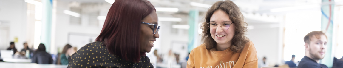 Two students talking in a large open plan study area.