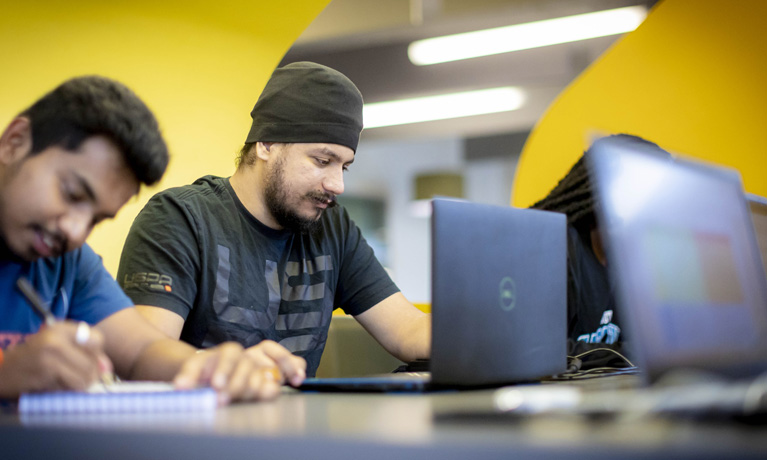 Male students working on laptops in a pod in The Hub on campus.