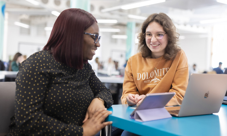 Two students smiling while working on a laptop.