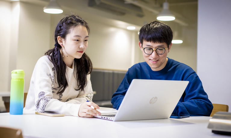 Two international students working on a laptop in a study space.