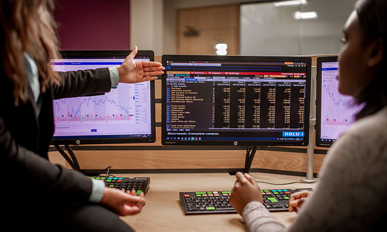 Two students looking at a bank of screens with lots of data displayed