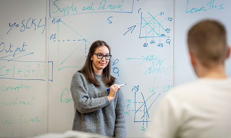 Two people against a whiteboard with blue writing on