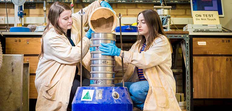 Two students wearing lab coats using geotechnics lab facilities