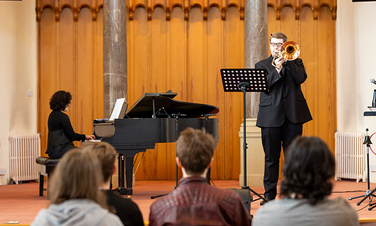 Student playing trumpet on stage accompanied by a pianist.