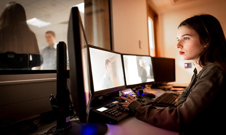 Woman inside the observation suite at desk with three monitors