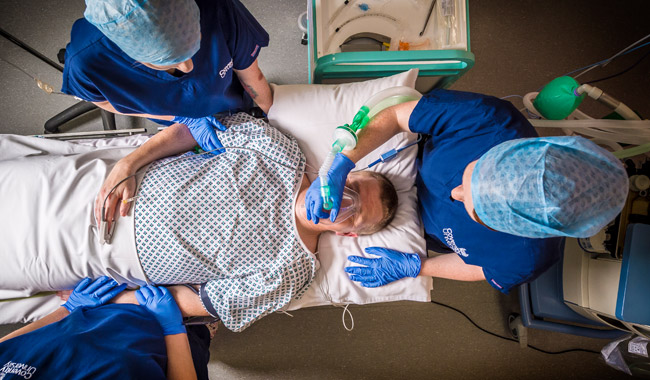 An operating department student holding an oxygen mask over a patients' mouth in a mock operating theatre.