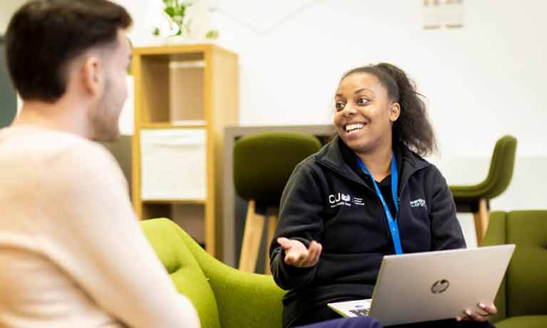 Student advisor with a laptop on her lap in conversation with a student