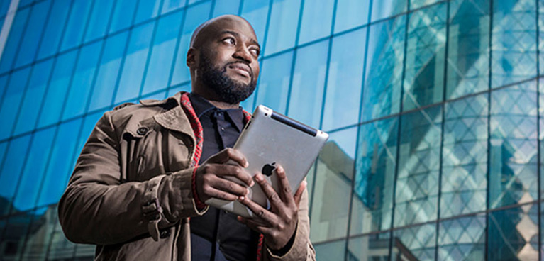 man walking along a street with tablet in this hand