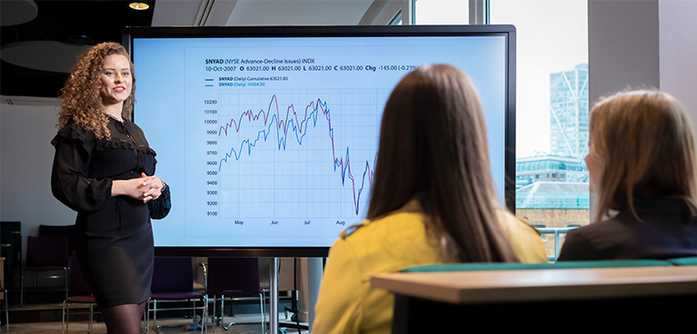 female student standing in front of a screen presenting to two students