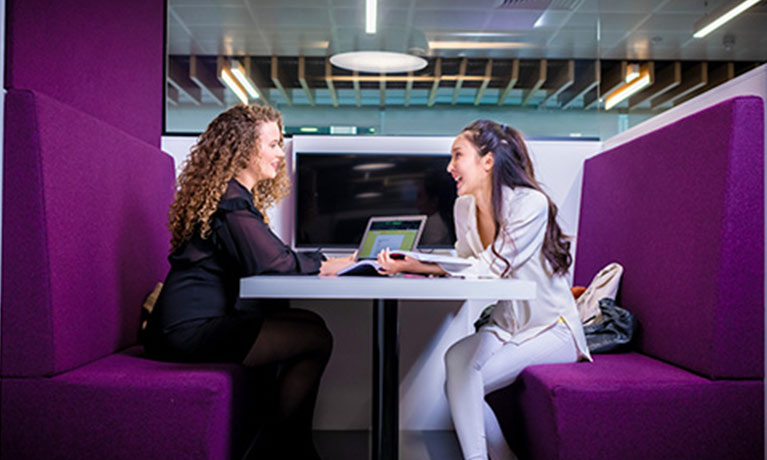 Two female students chatting across a desk