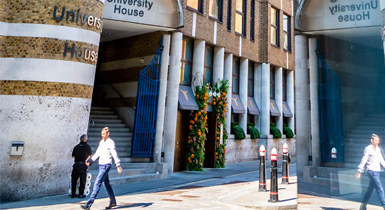 A man walking past Coventry University London's University House building on a bright sunny day
