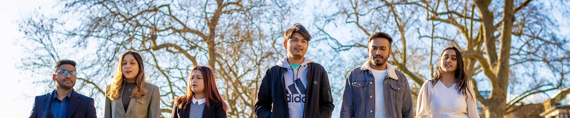 Five students walking outside with trees in the background