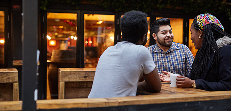 2 males and a female sitting outside a cafe chatting