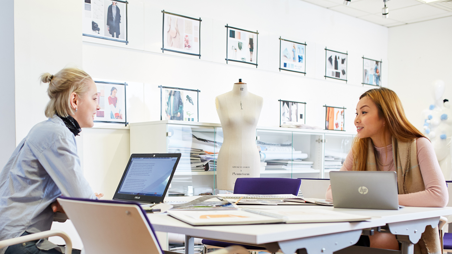 Two women looking at designs on laptops in a bright studio