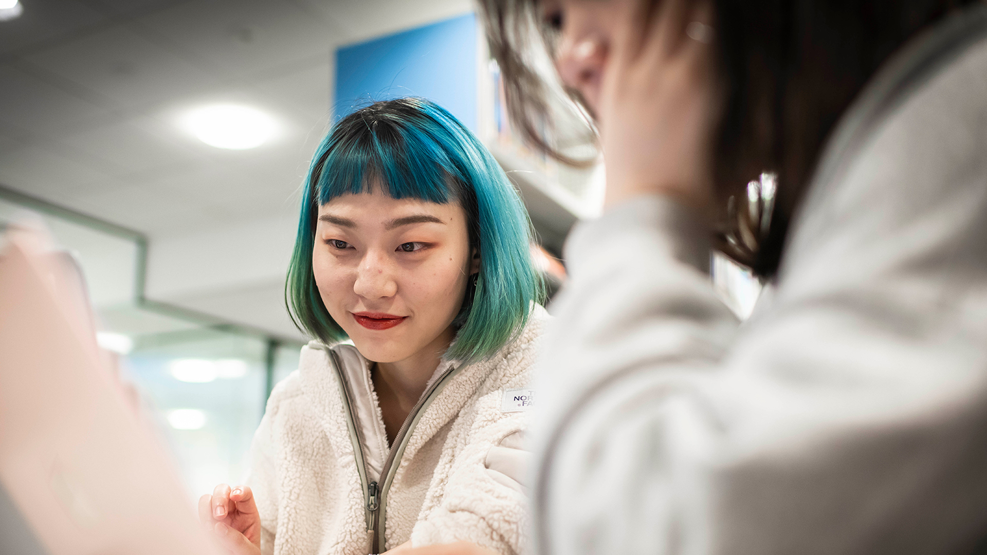 Young student with green hair talking to another female colleague