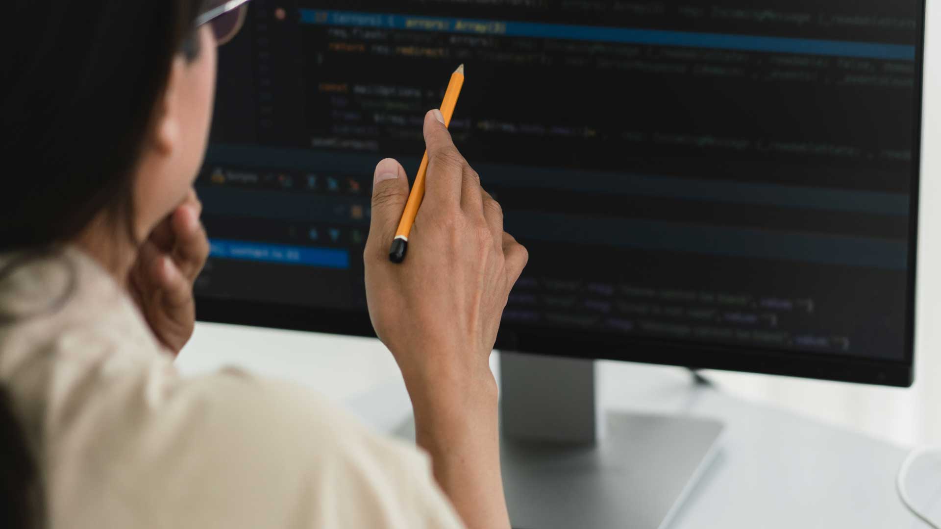Developer programmer holds pencil and checking code on monitor while programming to developing web