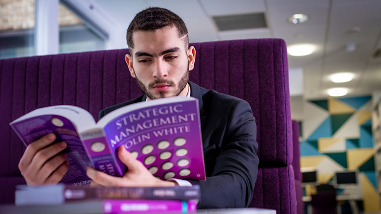 Male student reading a text book in a booth 