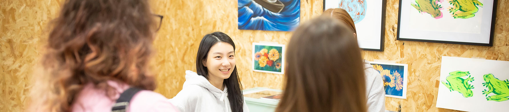 A smiling student with artwork behind here talks to visitors