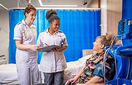 Two student nurses talking to a mock patient in a mock hospital bay 