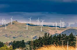 Hilly landscape covered with wind farm turbines with a dark cloudy sky in background