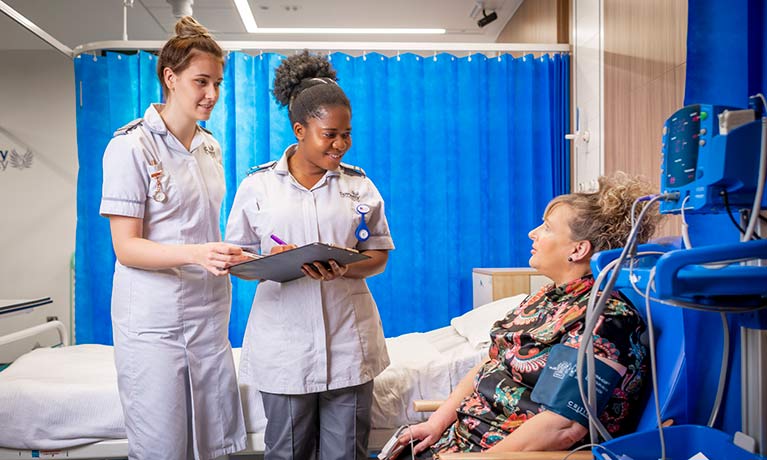 Two student nurses talking to a mock patient in a mock hospital bay 