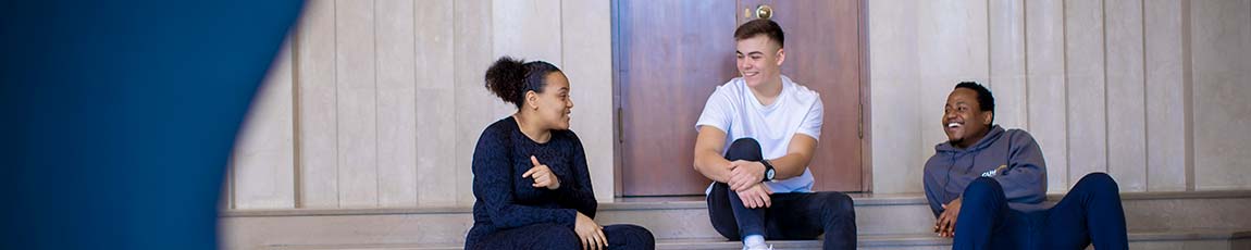 Three students sat on a step inside a building talking