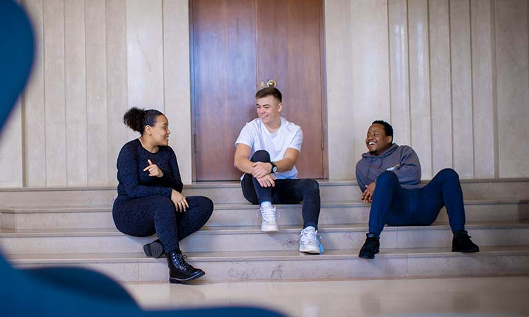 Three students sat on a couple of steps talking