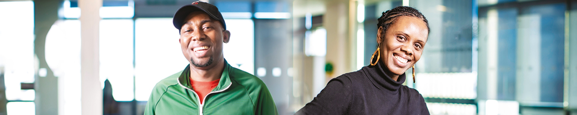 Two students stood in front of a glass wall smiling