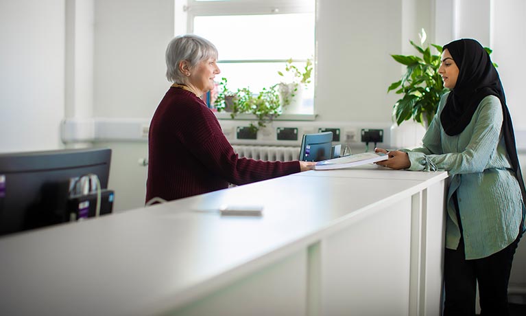 Student and member of staff stood at a reception desk talking