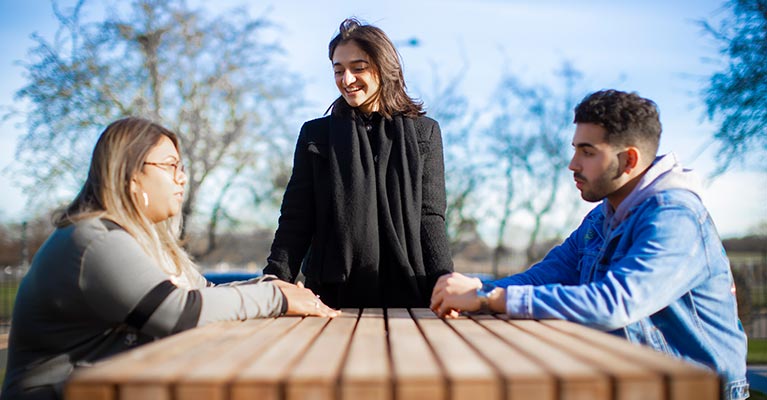 Three students standing around a table outside 