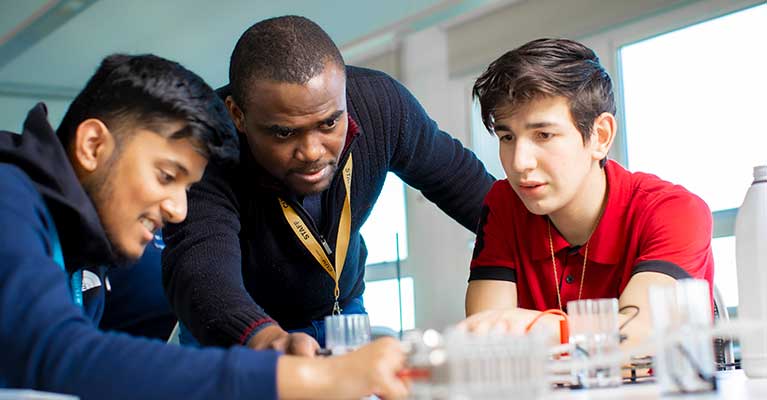 A male lecturer helping two male students with their work