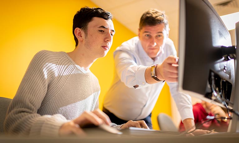 Lecturer standing over a student pointing towards the computer screen